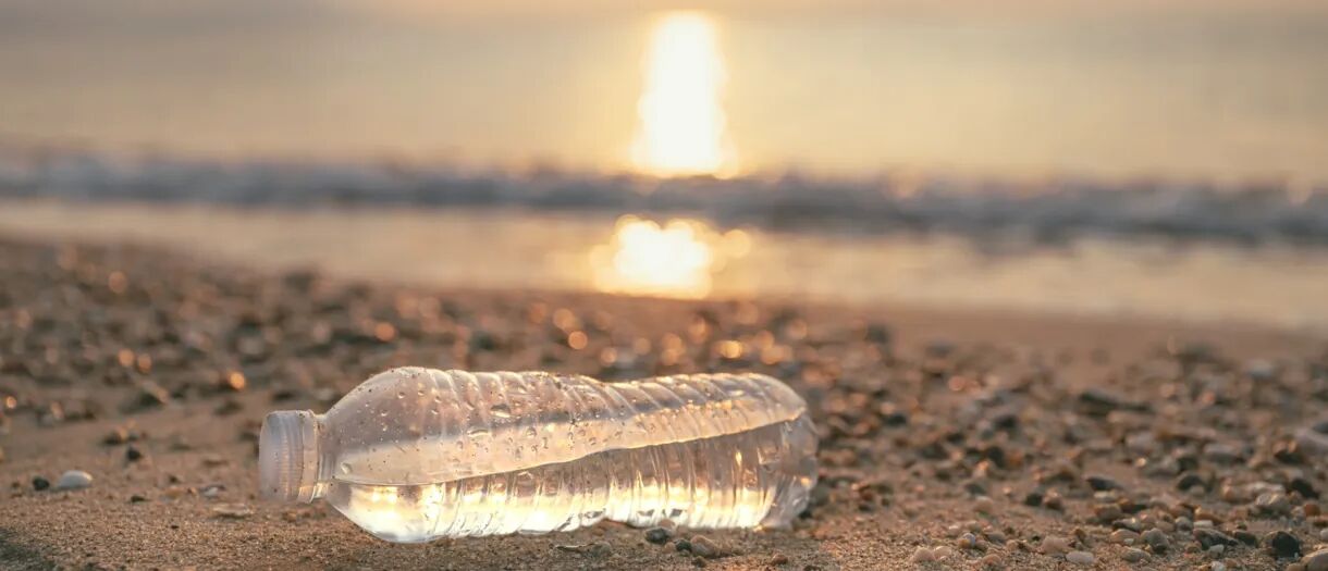 Een halfvolle plastic waterfles ligt op een zandstrand bij zonsondergang.