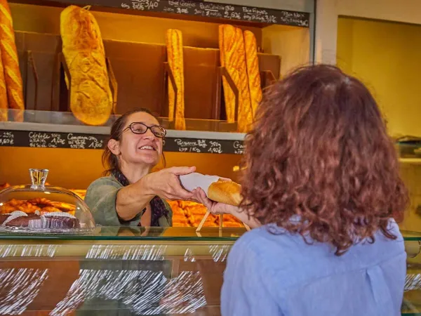 Een dame haalt stokbrood bij de bakker op Roan camping Les Dunes.