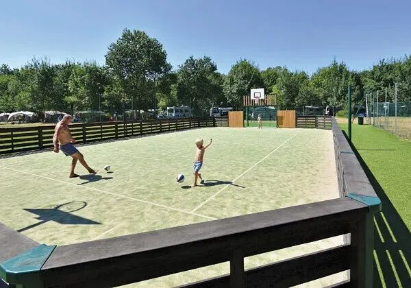Vader en zoon voetballen op het voetbalveld op Roan camping Domaine de La Brèche.