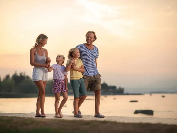 Lachende familie die aan het lopen is op het strand bij zonsondergang.