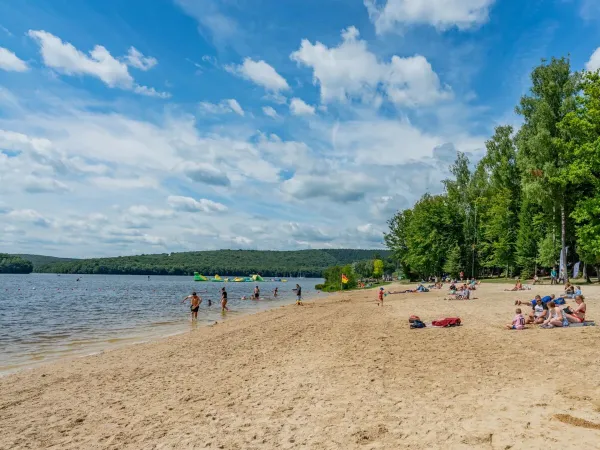 Families zonnen op het strand van het meer op Roan camping Le Lac des Vieilles Forges.
